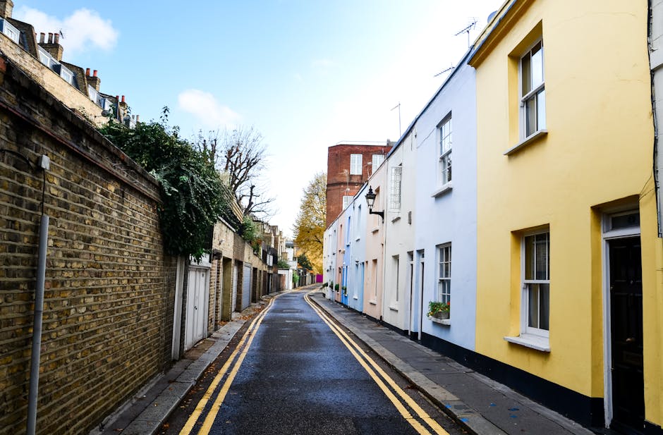 A narrow alleyway between two brick buildings in an urban setting, with a paved surface marked by double yellow lines along each edge. The left building features red brick walls with small, evenly spa